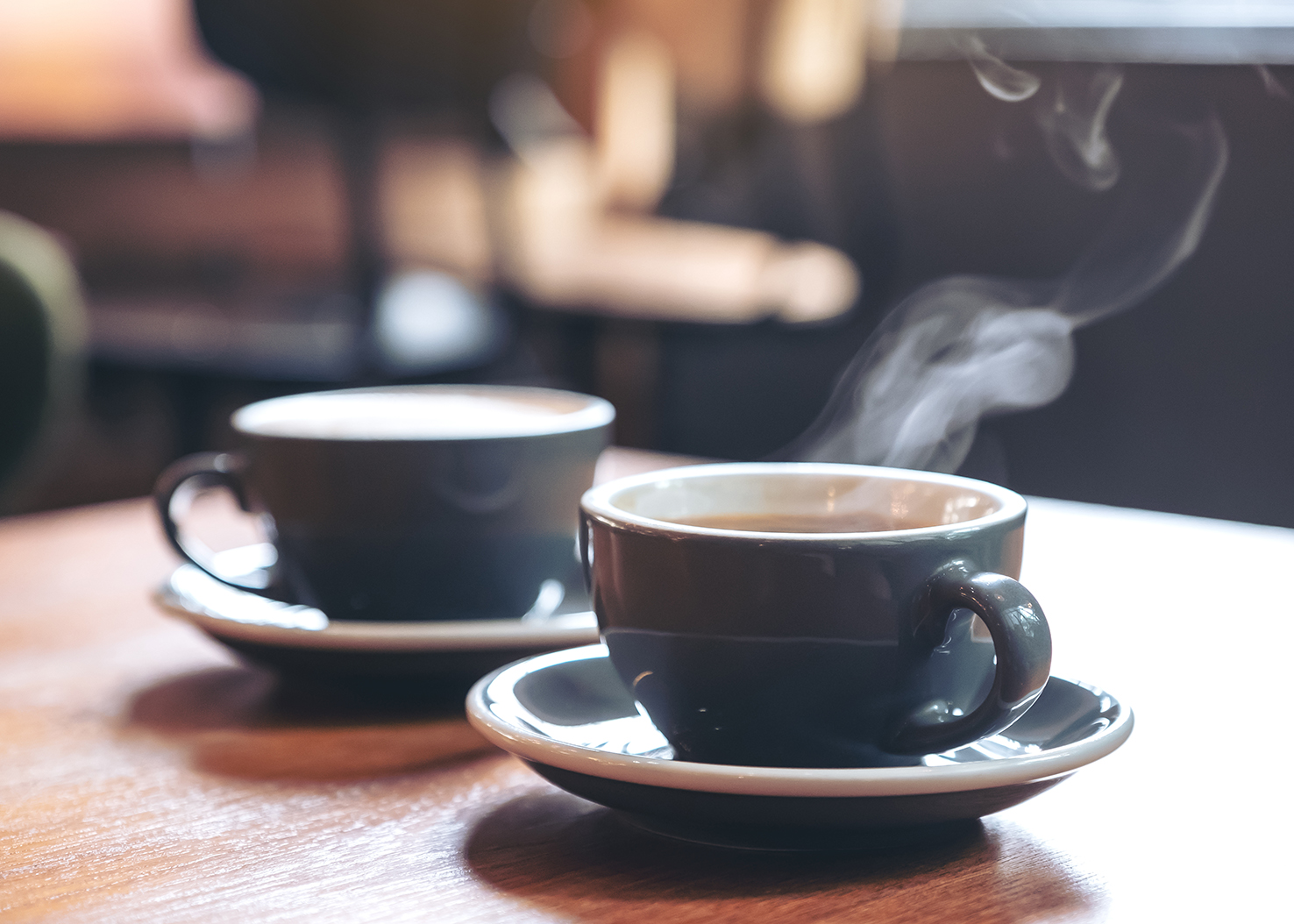 Closeup image of two blue cups of hot latte coffee and Americano coffee on vintage wooden table in cafe